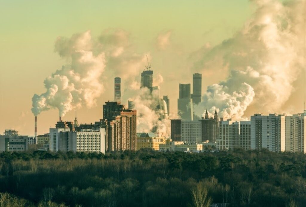 A city skyline featuring skyscrapers and smokestacks emitting smoke represents a polluted environment people who experience environmental injustice may live in.