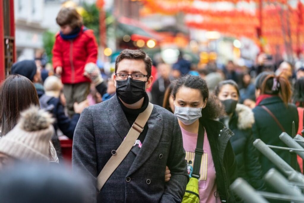 A man and woman wearing face masks walk together through a crowded street in China.