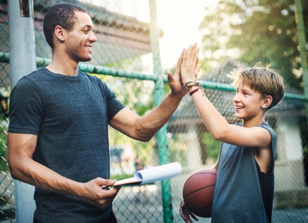 A public health educator high fives a young boy holding a basketball.