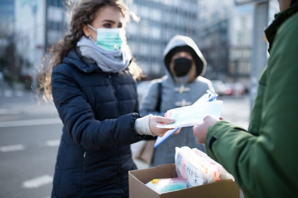 A woman hands out face masks to people walking by.