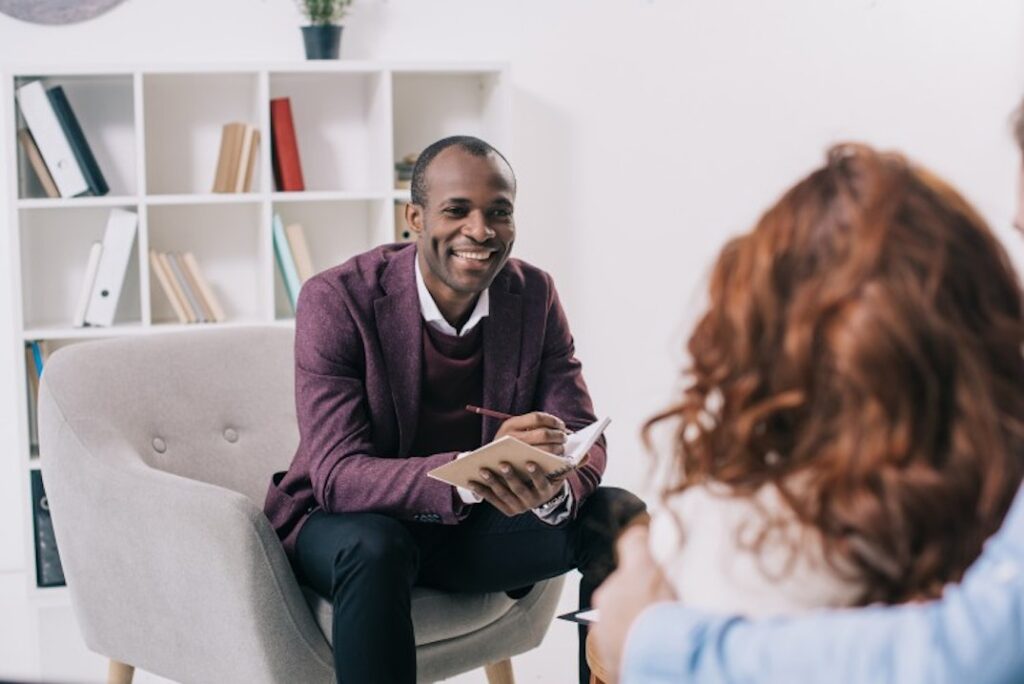 A therapist holds a notebook and talks to a couple.