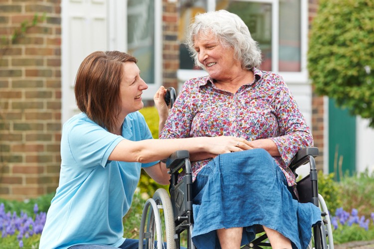 A healthcare advocate supports an older patient in a wheelchair