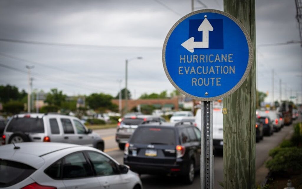 Cars line up on a road near a sign reading, “Hurricane Evacuation Route.”