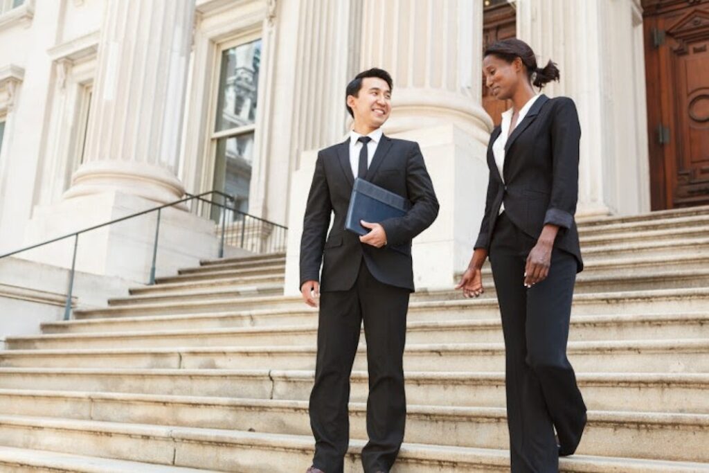 Two people in business attire walk down the steps of a courthouse.