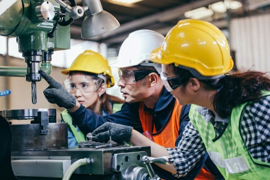 Three people in protective gear inspect the safety of an industrial machine.