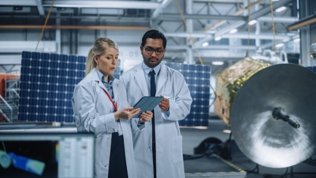 Two industrial hygienists in a factory discuss data while looking at a tablet computer.