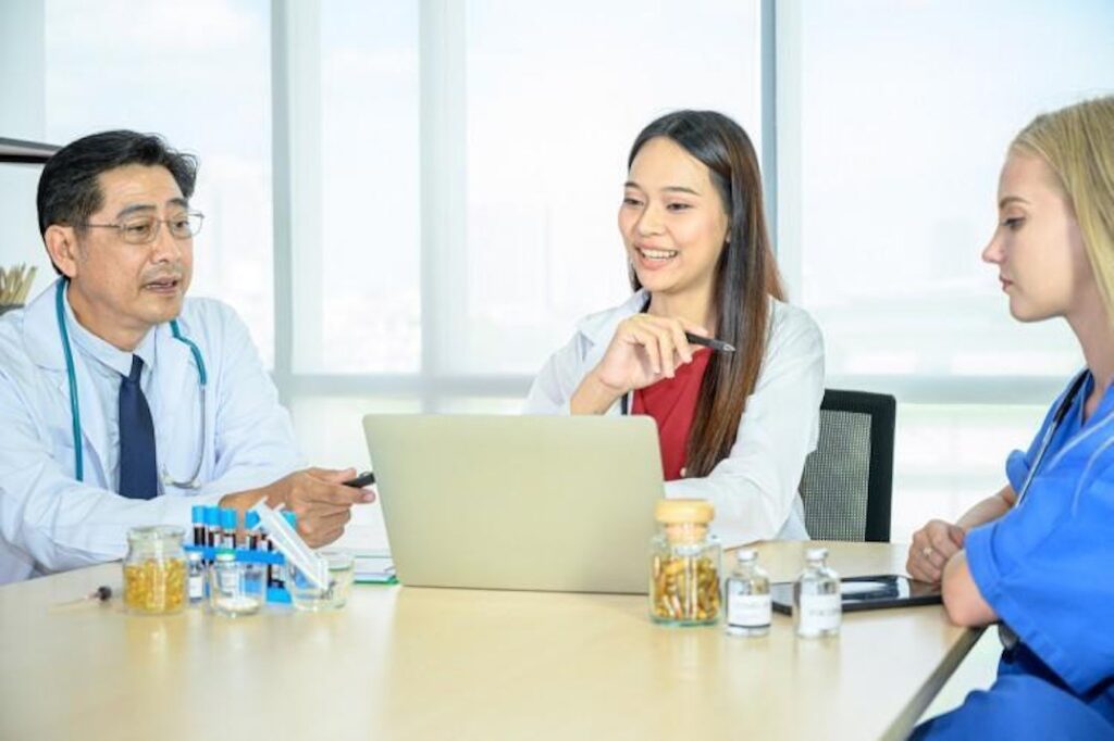 Three people in medical attire meet at a hospital conference table.