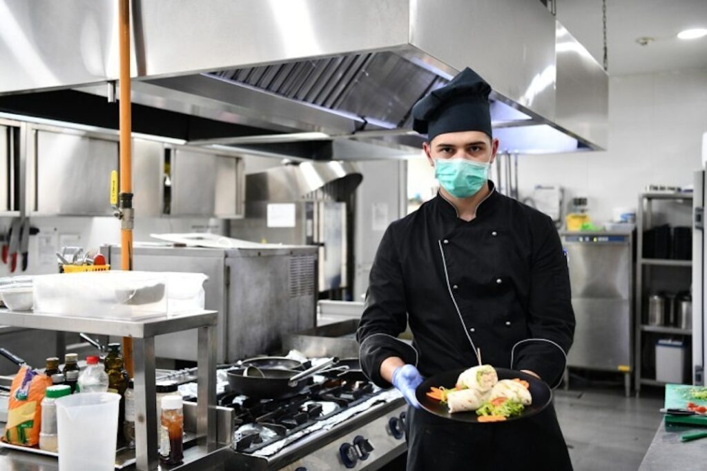 A cook in a restaurant kitchen holding a plate of food practices restaurant safety.