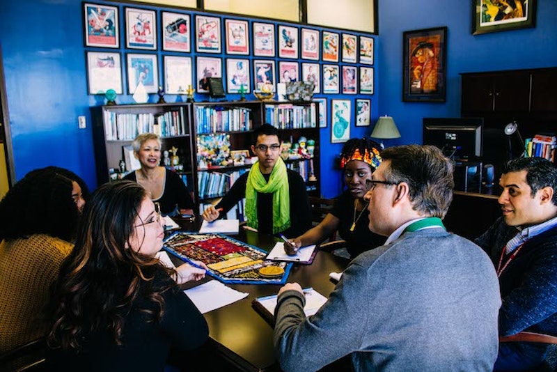 A group of Tulane University Online MHA students sit around a table with notebooks and pens