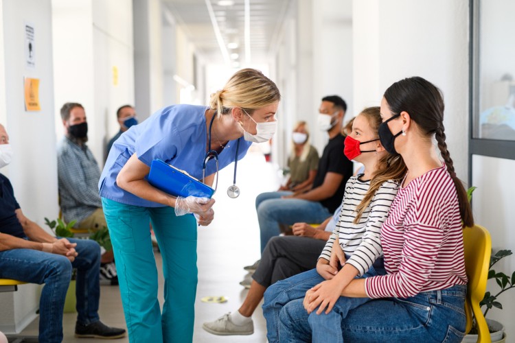 A nurse assists patients seated in a healthcare facility corridor.