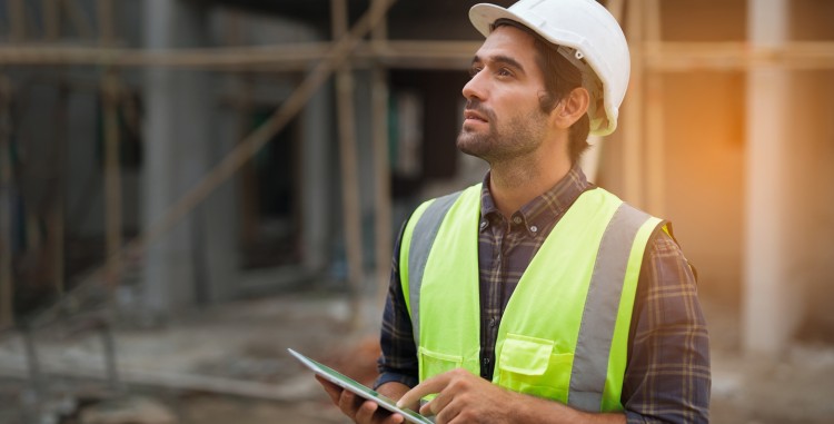 A safety inspector holds a tablet at a construction site.