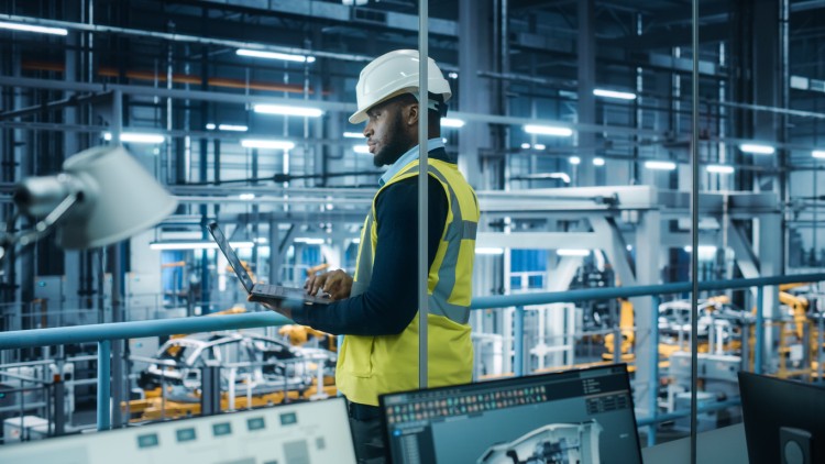 A safety director with a laptop looks down at a factory floor.