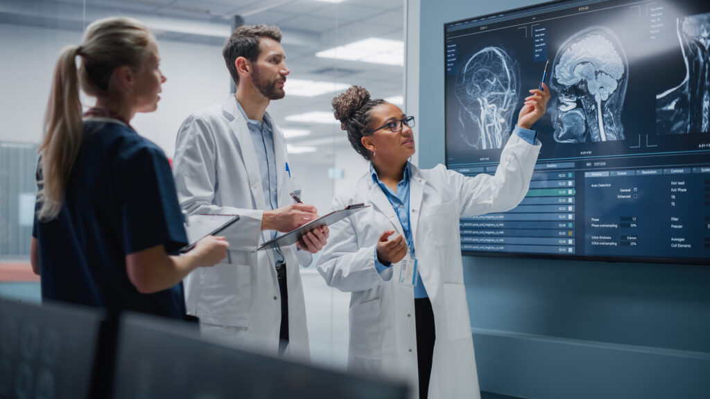 Three team members in a hospital lab discuss a screen display